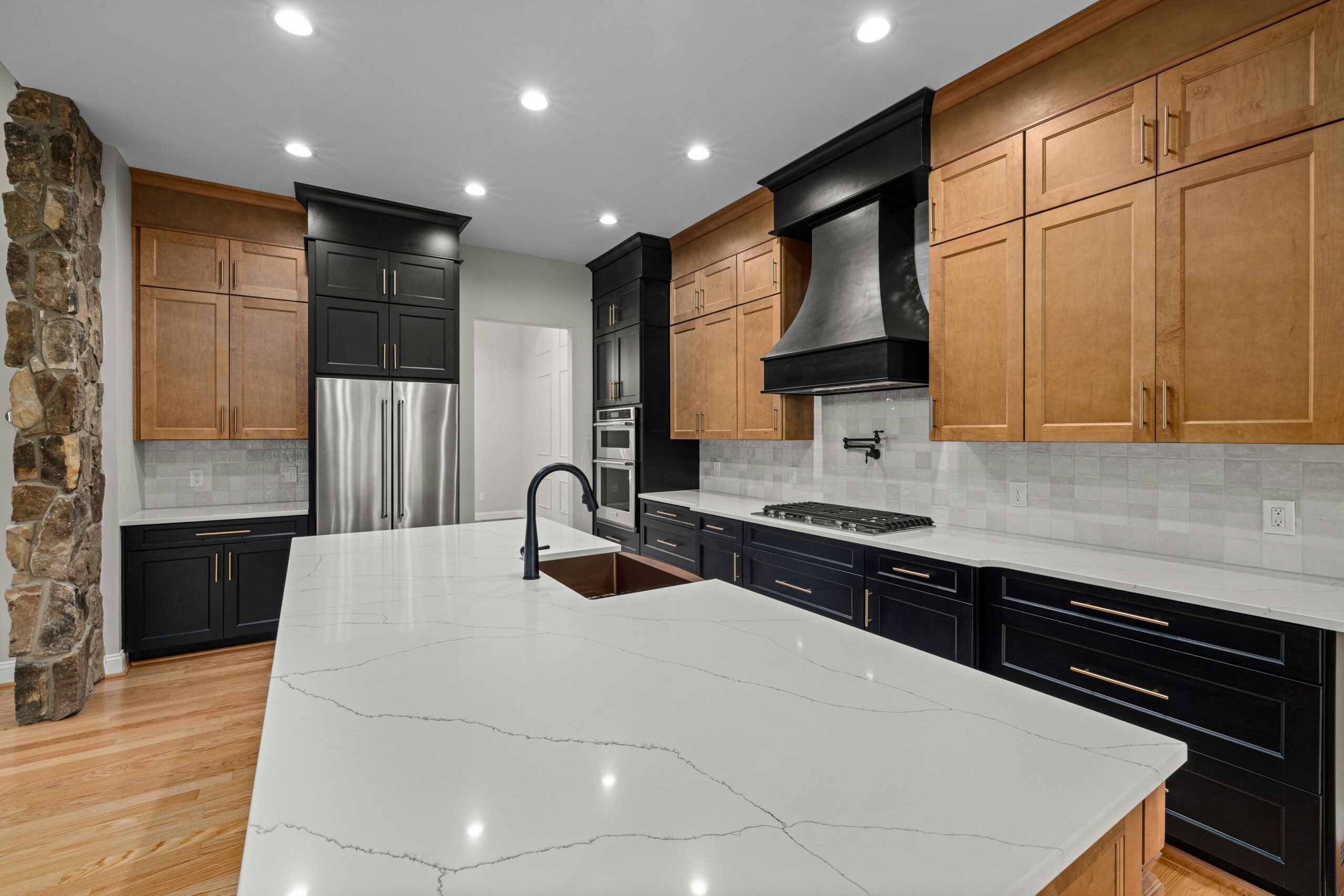 A kitchen has wooden cabinets and black cabinets paired with marble countertops for a luxurious aesthetic.