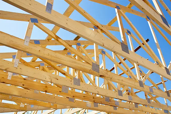 A roof under construction has trusses visible against a blue sky.