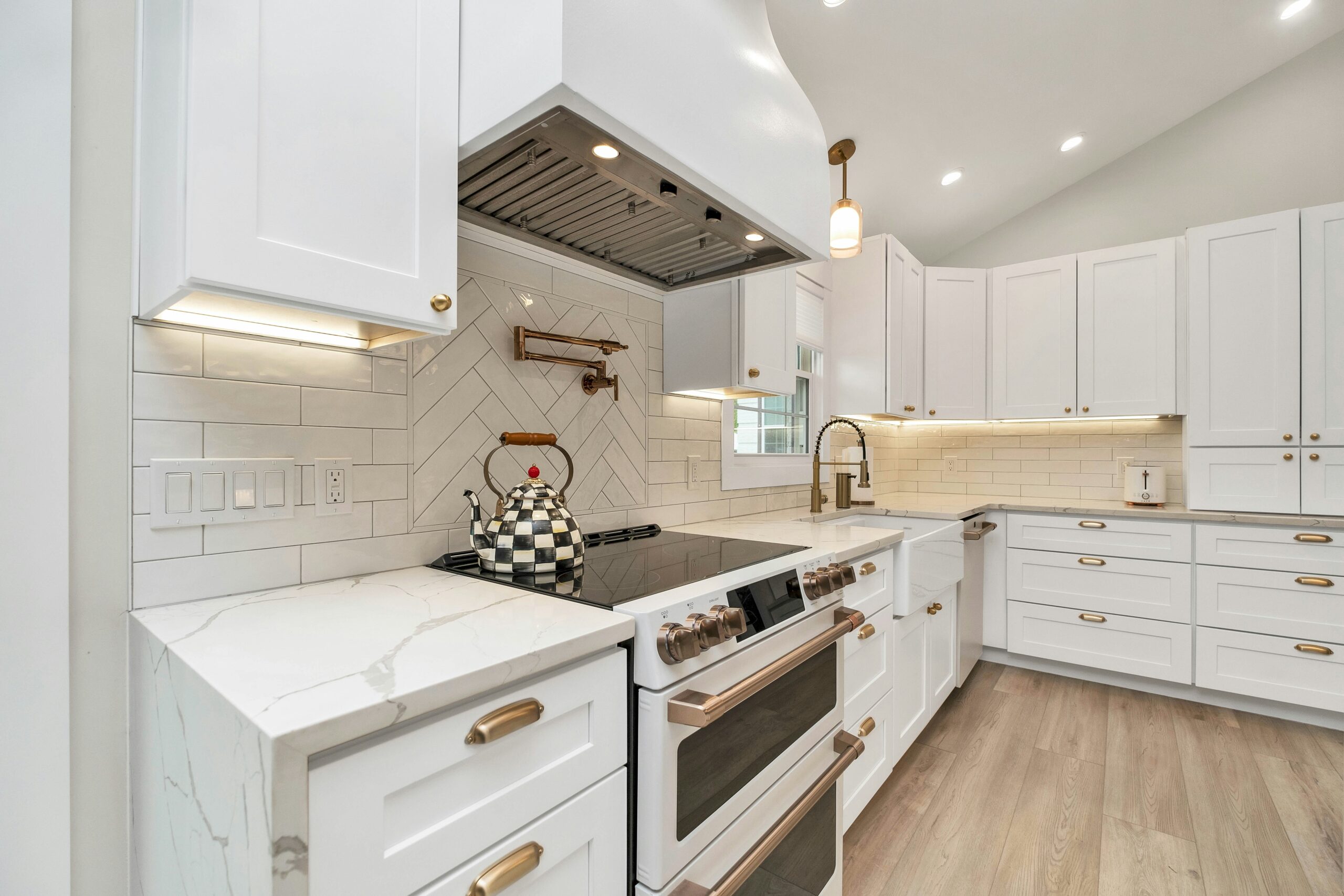 A stunning, modern kitchen has white cabinets, a tiled backsplash, quartz countertops and bronze hardware.