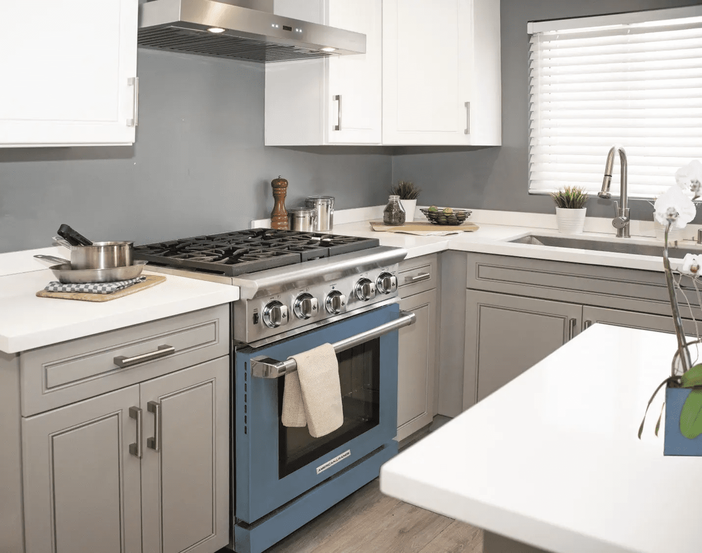 A modern kitchen has white countertops, grey cabinets and an eye-catching blue oven.