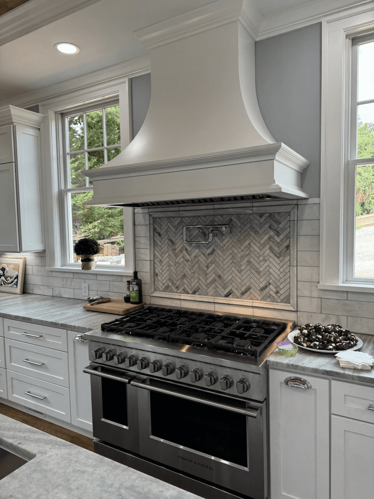 A modern kitchen has marble countertops, a tiled backsplash, a stainless steel oven and chrome hardware.