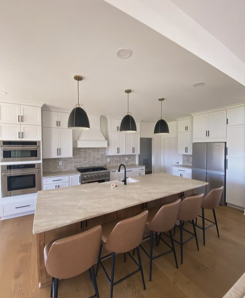 An elegant, spacious kitchen has white cabinetry, marble countertops, a wooden island, black hanging lights and stainless steel appliances.